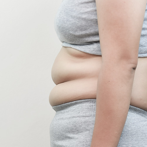 Close-up of a person measuring their abdomen with a yellow measuring tape while wearing a grey sports bra.