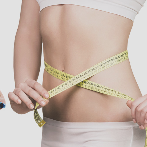 Close-up of a person measuring their waist with a yellow measuring tape while wearing white shorts.