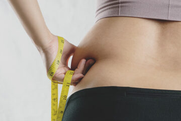 Person measuring waistline with tape measure after struggling with weight loss