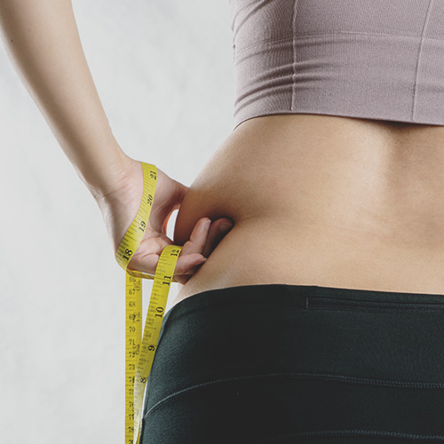 Person measuring waistline with tape measure after struggling with weight loss