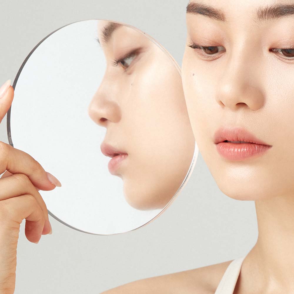 Close-up of a woman's face looking into a mirror reflecting smooth and clear skin.