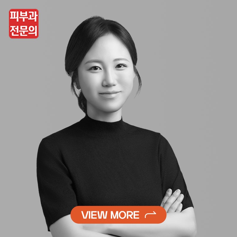 Portrait of a calm Asian woman in a black top, grayscale photo, with a red dermatology expert logo in the top-left and an orange 'VIEW MORE' button overlay.
