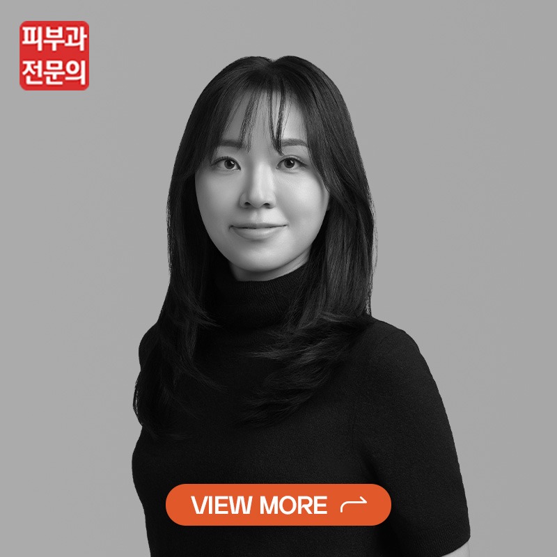 Portrait of a Korean woman in a black turtleneck, grayscale, suggesting a dermatologist on a skincare site with a red logo in the top-left and a yellow-orange 'VIEW MORE' CTA button.