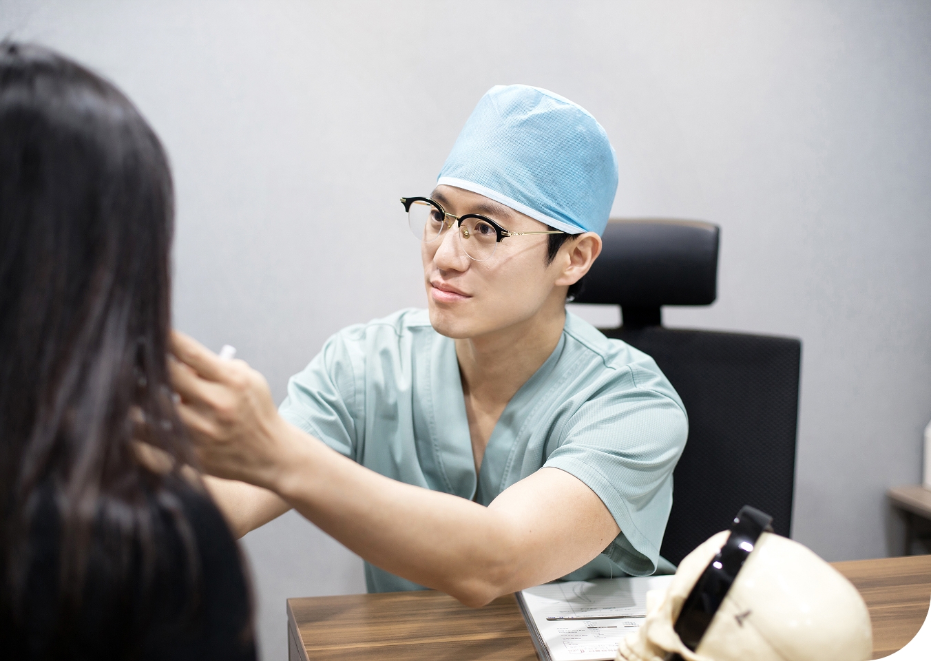 Dr. Jun Hyung Park who is skilled plastic surgeon in scrubs and a surgical cap consultation with a female patient in a clinic office, discussing potential procedures.